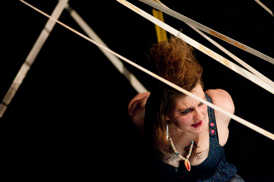 Actress performing in a web of slacklines during a theater production.